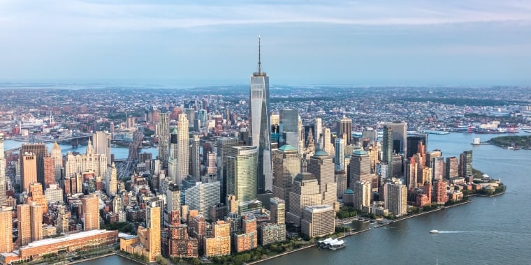 Aerial view of a downtown Manhattan skyline with tall buildings and skyscrapers, surrounded by water, under a cloudy sky.